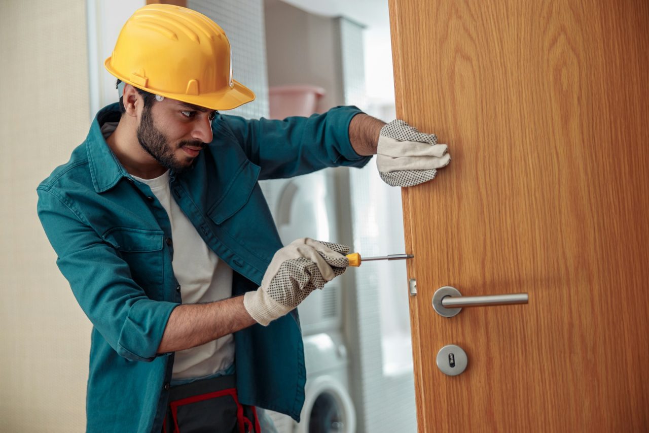 Homme avec un casque jaune qui répare une serrure avec outil